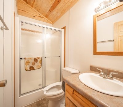A small bathroom with a wood ceiling, a shower with sliding glass doors, a towel hanging on the shower, a toilet, a sink with a countertop, and a mirror above the sink.